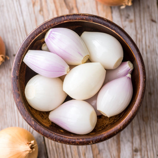 Peeled shallots in a brown bowl on a wooden table