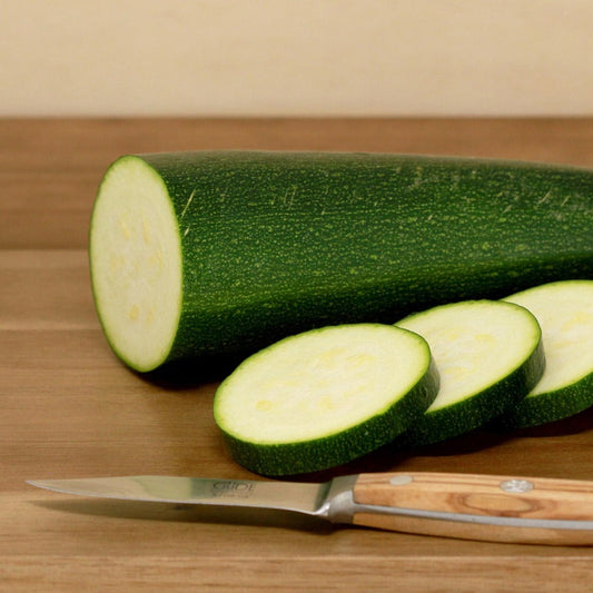 Sliced courgette next to a knife on a wooden chopping board