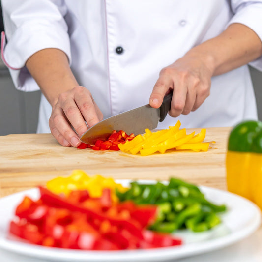 Chef slicing red, green and yellow capsicum into batons