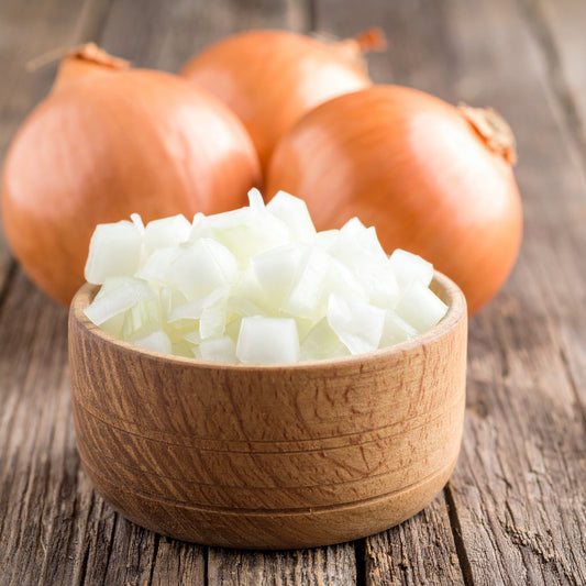 A wooden bowl filled with diced onions, with whole onions visible in the background against a rustic wooden backdrop.