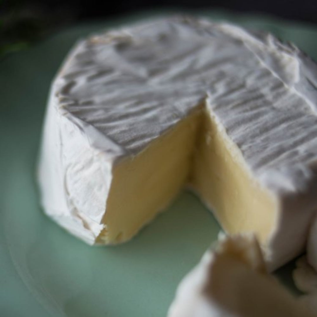 Round cheese with a slice removed on a green plate