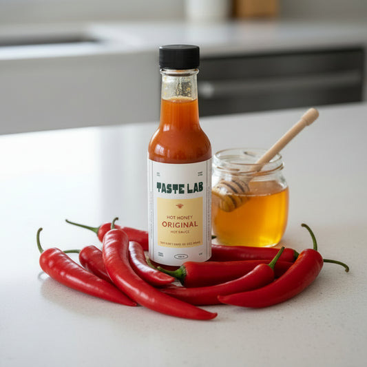 Bottle of Taste Lab Hot Honey Original hot sauce in a modern kitchen surrounded by chilies and honey.